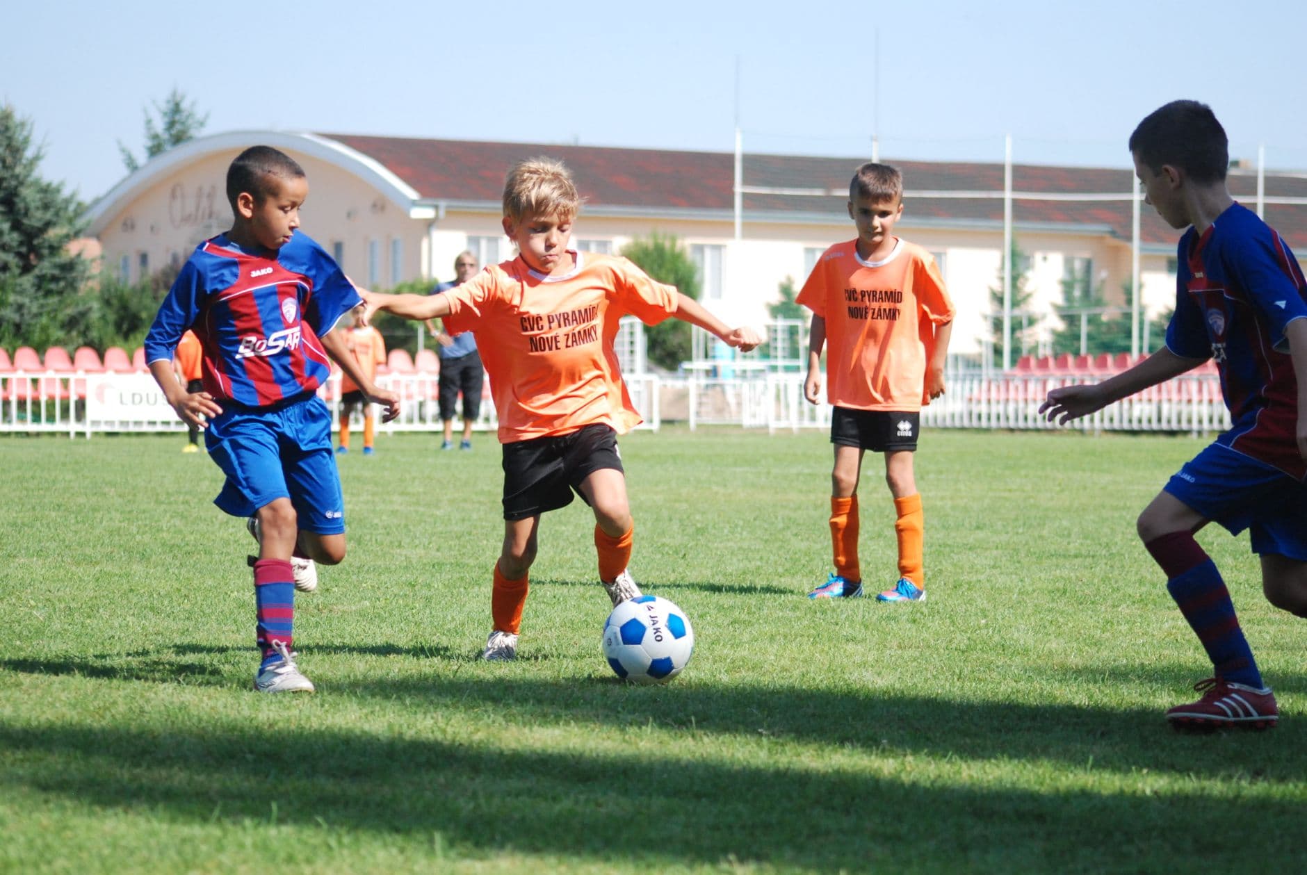 Children in football kits chasing the ball during a match on a grass pitch.