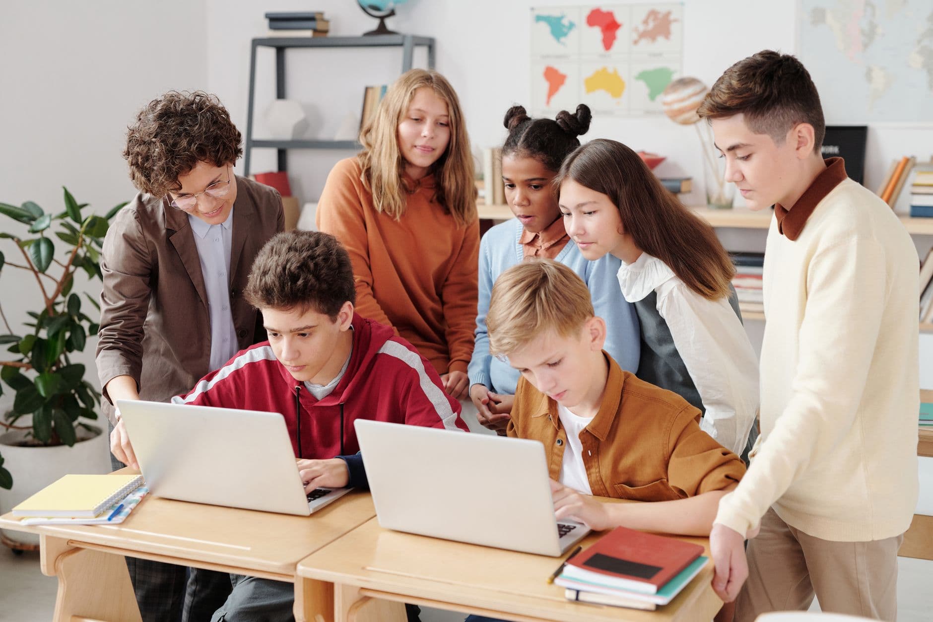 A group of secondary school students working together around laptops in a classroom.